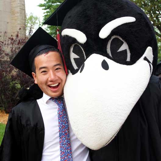 A graduate posing with Rocky the Raven